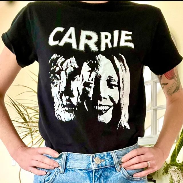 Black t-shirt with 'CARRIE' and a graphic of two faces, worn by a person.